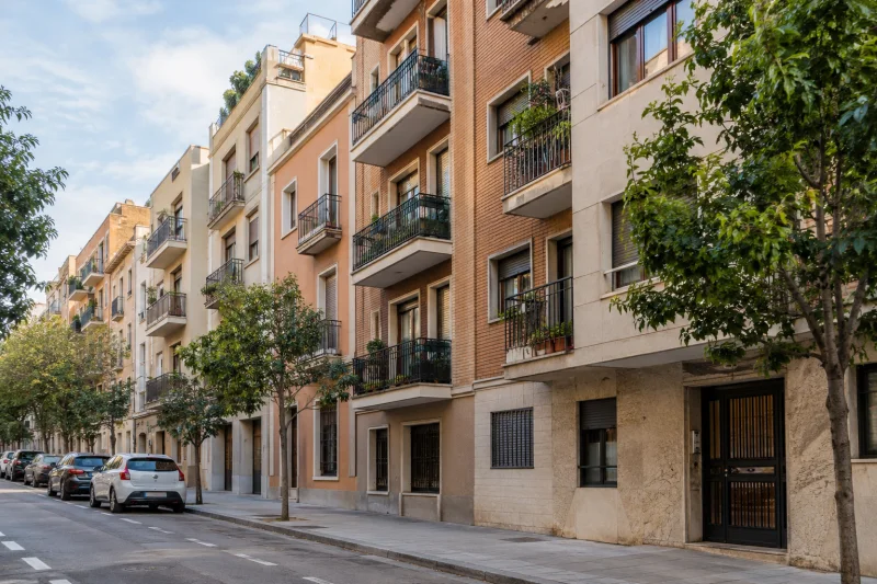 Edificios residenciales con balcones y árboles junto a una calle urbana