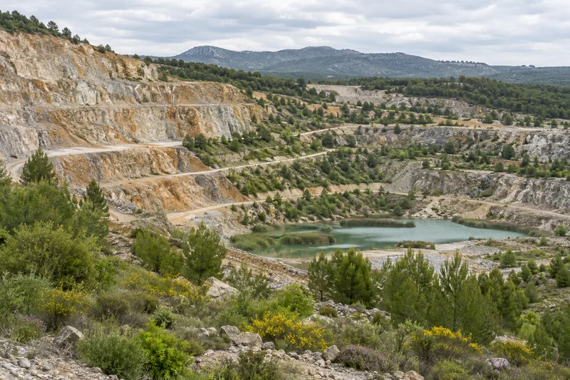 Terrazas de una cantera con vegetación y una lámina de agua al fondo.